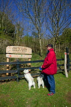 Visitor with dog looking at sign of Bishops Wood Local Nature Reserve, Murton, Swansea, Wales, UK 2009