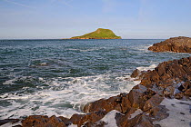 Limestone rocks washed by waves with the Worm's head in the background, cut off from the mainland as an island at high tide, Rhossili, The Gower peninsula, Wales, UK, July. Sequence 2 of 3 at differen...