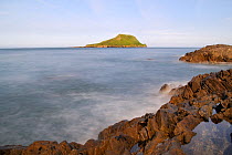 Long exposure view of limestone rocks washed by waves with the Worm's head in the background, cut off from the mainland as an island at high tide, Rhossili, The Gower peninsula, Wales, UK, July. Seque...