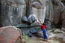 Pilgrim carrying out morning cleaning ritual on a carving of Shiva at 7th-9th century Hindu sacred site. Unakoti, Tripura, India, March 2012.