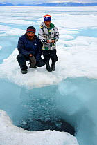 Inuit man showing his son the breathing hole of a Bearded seal (Erignathus barbatus) on the ice floe, Ellesmere Island, Nanavut, Canada, June 2012. Model released.
