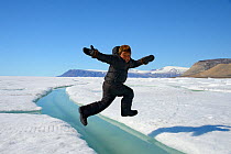 Young Inuit boy jumping over a crack on ice floe, Ellesmere Island, Nanavut, Canada, June 2012. Model released.