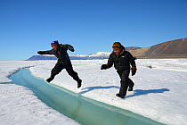 Two young Inuit boys jumping over a crack on ice floe, Ellesmere Island, Nanavut, Canada, June 2012.