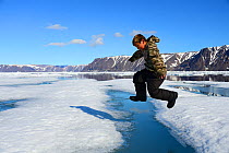 Young Inuit boy jumping over a crack on ice floe, Ellesmere Island, Nanavut, Canada, June 2012.