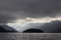 Looking up Bowen Channel with heavy cloud and moody lighting in the morning, with mountains covered in native forest, Dusky Sound, Fiordland, South Island, New Zealand