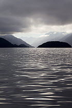 Looking up Bowen Channel with heavy cloud and moody lighting in the morning, with mountains covered in native forest. Dusky Sound, Fiordland, New Zealand.