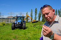 Slow worm (Anguis fragilis) being removed from brownfield site scheduled for development as part of mitigation project by Ecologist Brett Lewis, with tractor in background. Kent, UK, June 2012.