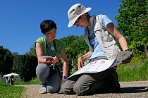 Volunteer Shen Yan Liow looks on as mammalogist Gill Brown refers to a mammal footprint identification chart during Arnos Vale Cemetery Bioblitz, Bristol, UK, May 2012 Model released.