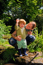 Young boy held by mother as he holds up a collecting pot after a pond-dipping session during Abbots Pool and woodland reserve Bioblitz, Bristol, June, Bristol, UK, June 2012. Model released.