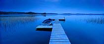 Wooden jetty on Carwitzer Lake with boat moored at night, Feldberger lake district, Germany, April
