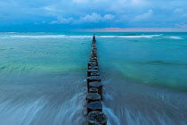 Waves washing around line of Wooden posts running into the Baltic Sea at dusk, National ParkVorpommersche Boddenlandschaft, Germany, May