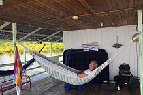 Photographer Doc White relaxing  in a hammock on a floating house on the Rio Negro, Amazonia, Brazil, June 2012