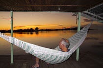 Photographer Doc White watching the sunset from a hammock, Rio Negro, Amazonia, Brazil, June 2012.