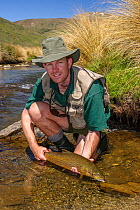 Portrait of fly fisherman (Michael Watson) holding a large brown trout (Salmo trutta) prior to release. Caught in a small spring fed stream, North Canterbury, South Island, New Zealand, December, 2003...
