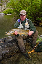 Fly fisherman (David Tasker) poses with a very good brown trout (Salmo trutta) prior to it's release, North Canterbury, Selwyn District, South Island, New Zealand. October, 2005. Model released.