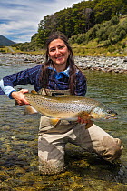 Female fly fisher with a 'trophy' brown trout (Salmo trutta) of 12 pounds (5.5kg), Lewis Pass, North Canterbury, South Island, New Zealand. December, 2005.
