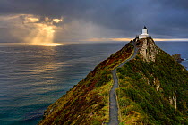 Nugget Point (Ka Tokata) lighthouse at sunrise, rain clouds sweeping on the horizon and crepuscular rays, Catlins, Clutha District, Otago, South Island, New Zealand. October, 2006.