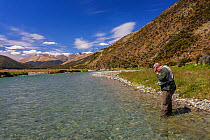 Fly fisherman (David Tasker) changes fly pattern on the Oreti River, Te Anau, Southland District, South Island, New Zealand. December, 2006. Model released.