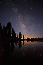 Lake with reflected stars of the Milky Way and silhouetted trees, Lassen Volcanic National Park, California, USA