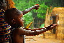 A bassari child holding out hands to collect rainwater, Bassari country,  east Senegal. This area became a UNESCO World Heritage site in 2012, for cultural landscape and traditions kept by the the Bas...