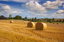 Stubble field and round straw bales after harvest with church tower in background, Glandford Norfolk, UK August