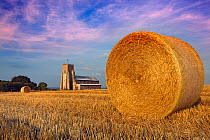Round straw bale in stubble field after harvest, with Salthouse Church in distance, Norfolk, UK, August