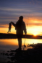 Arctic char (Salvelinus alpinus) catch held by silhouetted woman at sunset, 1002 coastal plain of the Arctic National Wildlife Refuge, North Slope, Alaska, USA