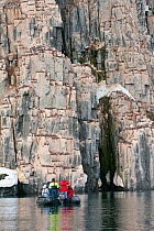 Colony of Brunnich's Guillemots (Uria lomvia) with tourist zodiac boat, Svalbard, Norway, June 2007