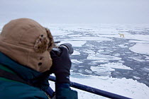 Man photographing Polar bear (Ursus maritimus) walking across ice sheet, Svalbard, Norway.