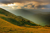 Sunlight shining through clouds onto alpine grassland of the Leota mountain range, Arges County, Carpathian Mountains, Romania, July, 2011