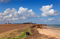 Walkers, lighthouse and church on coast, Happisburgh, Norfolk, UK, September 2012.