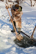 Gennadiy Kubolev, using a traditional Selkup shovel to remove pieces of ice from the water while checking a fishing net in a frozen river,  Krasnoselkup, Yamal, Western Siberia, Russia 2012