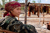 Rita Markova, a young Selkup woman, at a summer camp in the taiga, with animal pelts drying behind her, Krasnoselkup, Yamal, Western Siberia, Russia