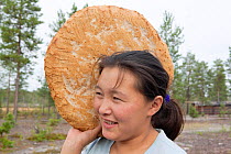 Lena Kuboleva, a young Selkup woman, holding a loaf of traditional Selkup bread she has baked in hot sand, at her family's summer camp in the forest, Krasnoselkup, Yamal, Western Siberia, Russia.
