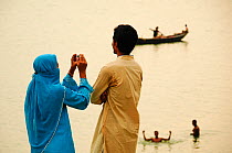 Man and veiled woman taking a photograph of the  River Ganges at sunset, Rajshahi. Bangladesh  June 2012. No release available.