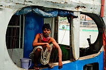 Man looking out from a boat at Sadarghat water front, Dhaleshwari river. Dhaka, Bangladesh. June 2012.