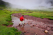Woman hiking  on a rainy day, crossing a river in the Aguas Tuertas in Hecho valley, Los Valles Occidentales Natural Park, Pyrenees, Aragon, Spain. Model released.