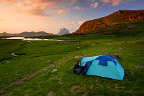 Hiker attending to tent while camping on Anayet alpine lakes. Midi d'Ossau peak in the background in Alto Gallego, Pyrenees, Aragon, Spain. Model released.