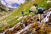 Women hiking,  crossing a stream in Remuae valley, Posets-Maladeta Natural Park, Pyrenees, Huesca, Aragon, Spain. Model released.