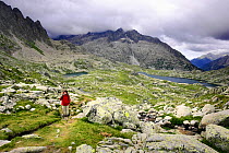Woman hiker  walking the 'Carros de Foc' trail at Cirque de Travessani with Punta Alta peak (3013 m), Boi valley, Aiguestortes i Estany de Sant Maurici National Park, Pyrenees, Catalonia, Spain. Model...