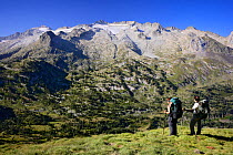 Two mountain walkers near La Picada pass, with Aneto Peak (3404 m) and Maladeta (3308 m) with its glaciers in the massif of Maladeta in the background, Posets-Maladeta Natural Park, Pyrenees, Aragon,...