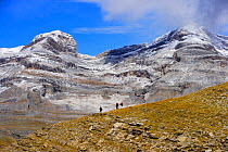 Mountain walkers below Cilindro de Marbora peak (3328 m) and Monte Perdido peak (3355 m), Ordesa and Monte Perdido National Park, Pyrenees, Huesca, Aragon, Spain