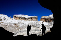 Two hikers silhouetted in Casteret ice cave with Brecha de Rolando / Roland's breach in the background, Ordesa and Monte Perdido National Park, Pyrenees, Aragon, Spain