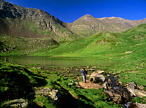 Hiker  with dog on the shores of Estany de Filia alpine lake in Vall Fosca, Pyrenees, Pallars Jussa, Catalonia, Spain. Model released