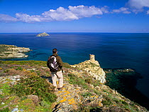 Hiker Oriol Alamany in Punta Agnello with the medieval tower and lighthouse, Cap Corse, Haute-Corse, Corsica Island, France. Model released