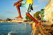Legs of local man jumping into the water from jetty in Port Stone, Zanzibar Town, Zanzibar, Tanzania