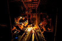 Camp life at Sombom Camp in the Saruwaged Range, Huon Peninsula. Photographer Tim Laman (front left) and ornithologist Ed Scholes (back left), and Papua New Guinean field assistants warm up at the fir...