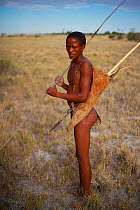 A young Zu/'hoasi Bushman carrying a bow, a quiver of arrows and a pole for hunting Spring Hares (Pedetes capensis) on the open plains of the Kalahari, Botswana. April 2012.