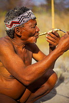 A Zu/'hoasi Bushman lights a pipe made out of an old artillery cartridge. Kalahari, Botswana. April 2012.