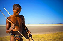 A young Zu/'hoasi Bushman hunter carrying a bow, quiver of arrows and a long pole for catching Spring Hares in their burrows. Kalahari, Botswana. April 2012. No release available.